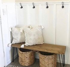 a wooden bench with two baskets underneath it and three hooks on the wall behind it