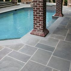 an outdoor pool with brick pillars and tiled flooring next to the swimming pool area