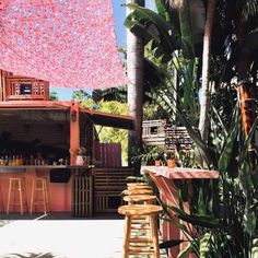 an outdoor bar with wooden stools and tables in the shade under a pink tarp