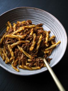 french fries in a white bowl with a wooden spoon on a black table top, ready to be eaten