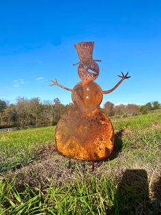 a rusted metal snowman sitting on top of a rock in the middle of a field