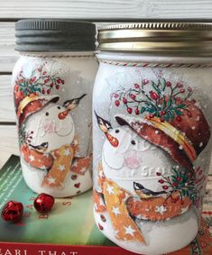 two decorated mason jars sitting next to each other on top of a book with christmas decorations