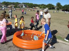 a group of people standing around an orange pool filled with water and plastic toys while children play in the background