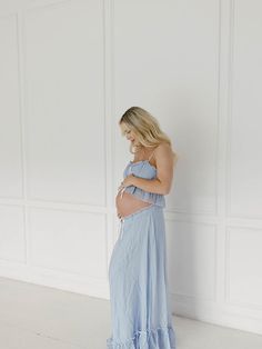 a pregnant woman in a blue dress leaning against a wall with her hands on her stomach