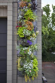 a tall planter filled with lots of different types of flowers next to a garage door