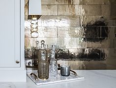 a kitchen counter with two glasses on it and a silver tray in front of the wall