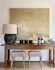 a wooden table topped with two stools next to a painting