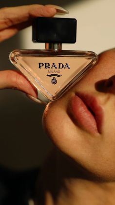 a woman looking at her perfume bottle with the word prada on it in front of her face