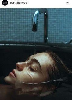 a woman laying down in a bathtub with water pouring from the faucet