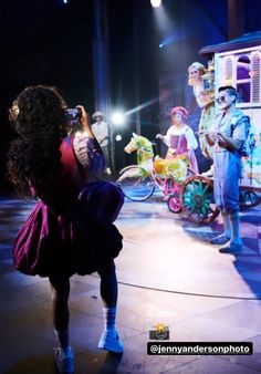 a woman taking a photo of children on stage with clowns in the back ground