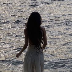 a woman is standing on the beach looking at the water with her back to the camera