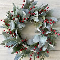 a christmas wreath with red berries and greenery on a white wooden background, ready to be hung