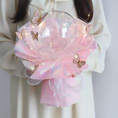 a woman holding a pink glass bowl with butterflies on the side and lights in it