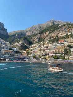 boats are parked on the water in front of some buildings and mountains with cliffs behind them