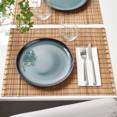 a place setting with blue plates and silverware on a woven place mat next to a plant