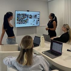 three women sitting at a table with laptops in front of them and one woman standing up