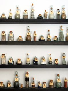 several shelves filled with bottles and vases on top of each other in front of a white wall