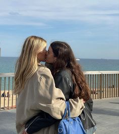 two women are kissing each other on the boardwalk by the ocean with their backs to one another