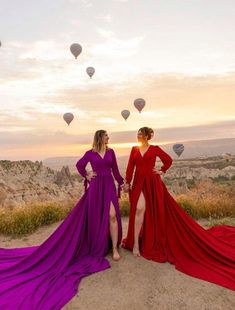 two women in long dresses standing on sand with hot air balloons