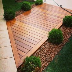 a wooden deck surrounded by green grass and shrubbery on the side of a house