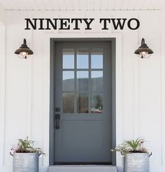 two metal buckets with plants in front of a gray door on a white house