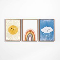 three framed art pieces hang on the wall above a white wall, each with an image of a sun, rainbow and cloud