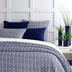 a bed with blue and white comforters in a room next to a potted plant