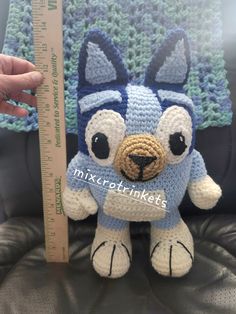 a crocheted blue and white stuffed animal next to a measuring ruler on a chair