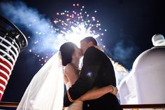 a bride and groom kissing on the deck of a cruise ship with fireworks in the background