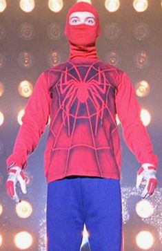 a man in a red spider suit and blue pants on stage with lights behind him