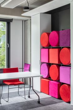 an office with pink, red and purple cubes on the wall next to a white table