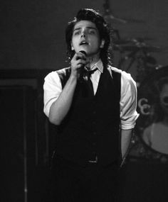 a man with black hair holding a microphone in his right hand and singing into the microphone