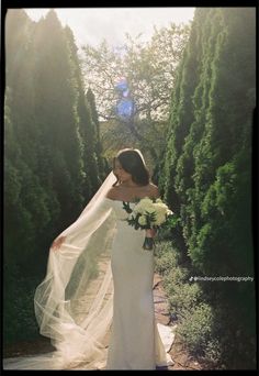 a woman in a wedding dress is holding a bouquet and posing for the camera with her long veil over her shoulder