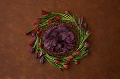 a bird's nest filled with purple tulips on top of a brown surface