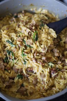 a pot filled with pasta and meat on top of a stove next to a wooden spoon