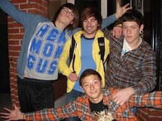 four young men posing for the camera in front of a brick building with their arms up