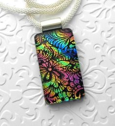 a necklace with a colorful design on it sitting on top of a white table next to a chain