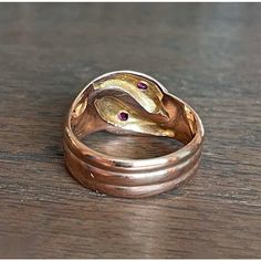 In the quiet, storied streets of Birmingham, 1918—a city teeming with industrious spirit and the echoes of a bygone era—a master goldsmith crafted this splendid creation. With its serpentine elegance, this ring features two serpents entwined in a dance of eternal allure. Each snake, rendered in lustrous 9 karat gold, showcases the hallmark of an era: the anchor for Birmingham and the letter 'T' denoting the year 1918, alongside the revered maker’s mark ‘H.W. Ld’. These symbols of authenticity promise not just a piece of jewelry, but a journey through time.  Adorning each serpent's head is a resplendent fuchsia-colored round faceted ruby measuring 2.6 mm across. These radiant gemstones capture the essence of a captivating twilight and reflect a world where opulence meets the extraordinary. Antique 14k Gold Hand Forged Rings, Antique Hand Forged Rings For Formal Occasion, Antique Hallmarked Snake Ring, Vintage Hand Forged Yellow Gold Rings, Hallmarked 14k Gold Snake Ring, 14k Gold Hallmarked Snake Ring, 14k Gold Hallmarked Snake Ring For Anniversary, Heirloom Hallmarked Snake Ring As Gift, Elegant Hallmarked Snake Ring