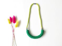 a green necklace next to two pink flowers on a white surface with a metal hook