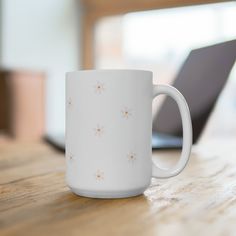 a white coffee mug sitting on top of a wooden table next to a laptop computer