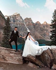 a bride and groom holding hands while standing on top of a rock in the mountains