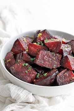 a white bowl filled with cooked beets on top of a table next to a napkin