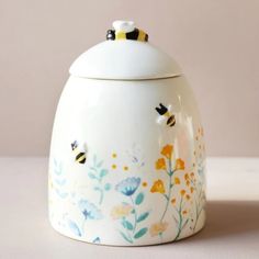 a ceramic jar with flowers and bees painted on the front, sitting on a table