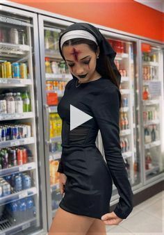 a woman in a black dress standing next to a refrigerator filled with drinks and sodas