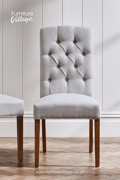 two grey chairs sitting side by side in front of a white wall and wooden floor