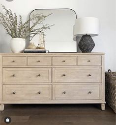 a dresser with a mirror, vase and lamp on it in front of a white wall