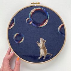 a hand is holding an embroidery hoop with a rat on it and bubbles in the air