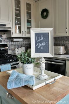 a kitchen counter with a chalkboard sign and potted plant on top of it