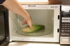 a person reaching into a microwave with an uncooked banana on the plate in it