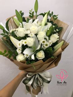 a bouquet of white flowers is being held by someone's hand in front of a wall